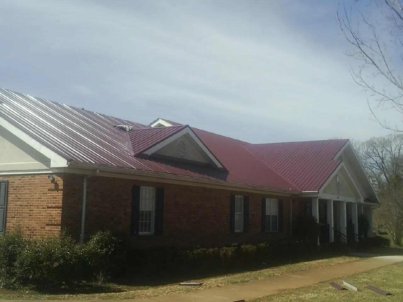 Red metal roof with gabled entries on a long brick building, from a Hail Damage Roof Repair job in Copalis Crossing