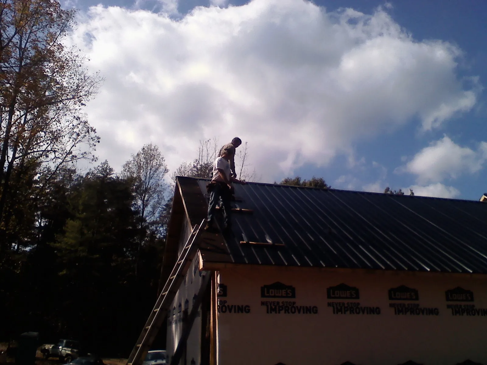 Roofer fastening dark metal panels high against a cloudy sky, from a Roof Inspection job in Copalis Crossing