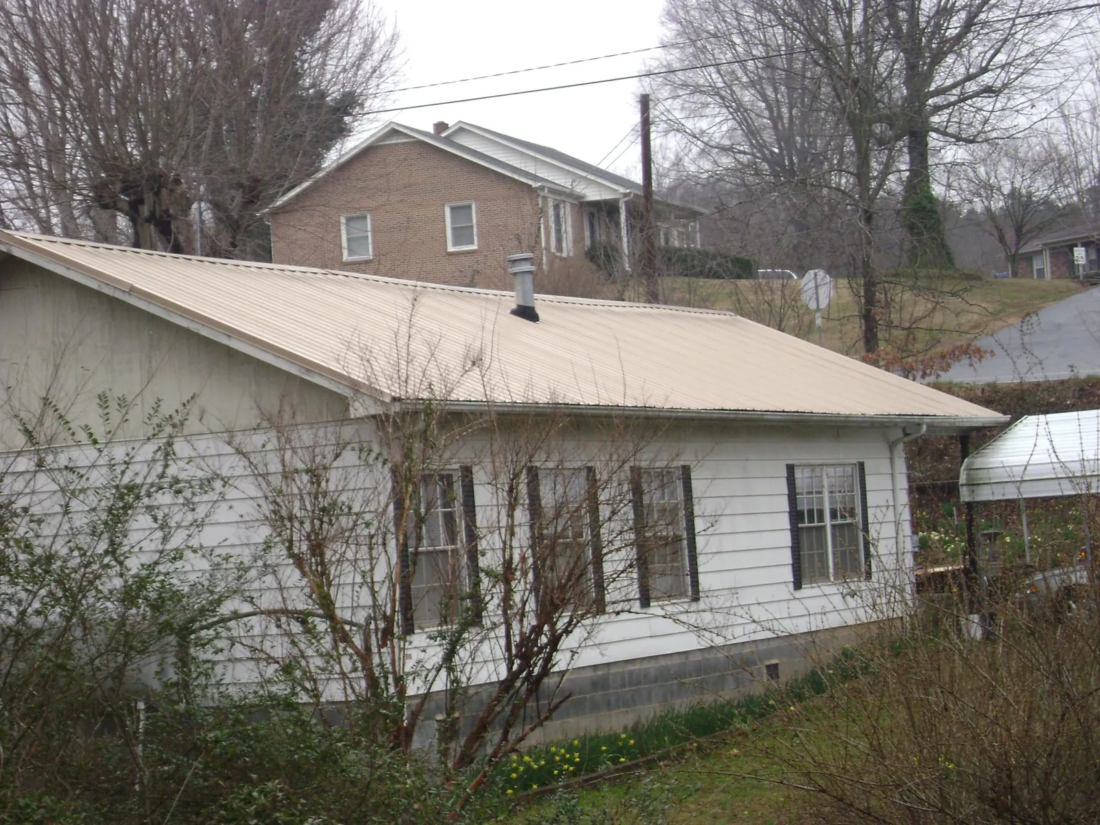 Tan metal roof on a white sided house set into a hillside — Commercial Roofing by Roofing Brothers in Copalis Crossing